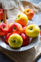 Top view of collection of ripe, colorful apples presented on a rustic wooden board, with a white plate, fork, and draped fabric creating a serene kitchen setting - ADSF49515