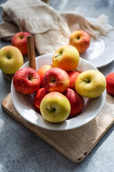 From above of collection of ripe, colorful apples presented on a rustic wooden board, with a white plate, fork, and draped fabric creating a serene kitchen setting - ADSF49518