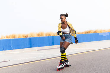 Full body of young African American woman rollerskating on rink at skate park against clear sky with lots of copy space - ADSF49558