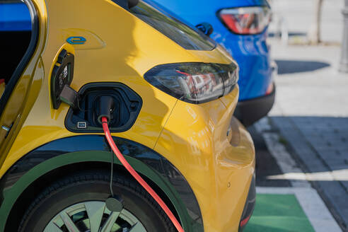 Close up view of a yellow electric car's charging port with a connected red cable at an outdoor station - ADSF49625