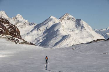 Full body back view of unrecognizable person with ski poles walking on snow covered mountain during sunny day at Swiss Alps - ADSF49642