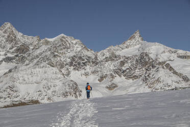 Full body back view of unrecognizable person with ski poles walking on snow covered mountain during sunny day at Swiss Alps - ADSF49643