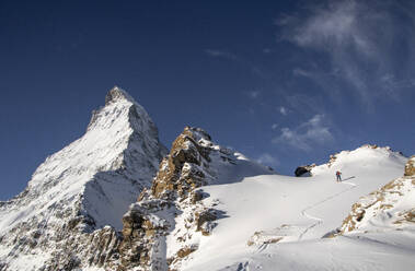 From below of back view of unrecognizable person with ski equipment walking on snow covered mountain slope during sunny day at Swiss Alps - ADSF49646