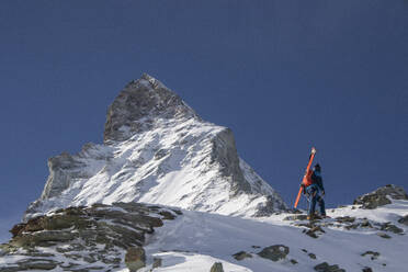 Unrecognizable person with ski equipment standing on snow covered mountain against clear blue sky at Swiss Alps - ADSF49648