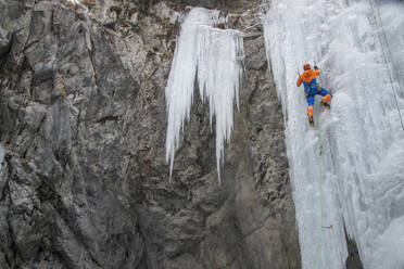 Back view of ice climber with ice axe climbing frozen waterfall on mountain during vacation at Swiss Alps - ADSF49650