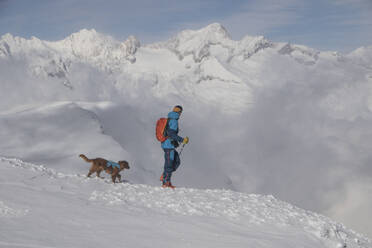 Side view of anonymous person hiking with pet dog on snow covered mountain during vacation at Swiss Alps - ADSF49657