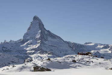 Majestic snow-covered mountain peak towering over traditional wooden cabins in a winter landscape - ADSF49662