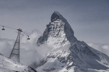 Low angle view of overhead cable cars by majestic mountain peak against sky during winter - ADSF49669