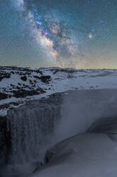 Majestic view of a stunning frozen waterfall cascading over a cliff edge, under a vibrant starry sky with the Milky Way visible, surrounded by snowy landscapes in iceland - ADSF49678