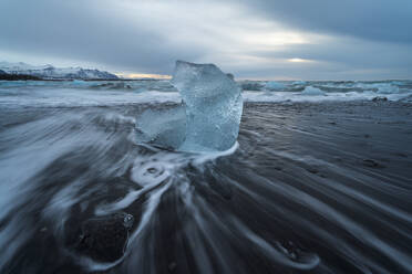 Picturesque scenery of rippling sea water with pieces of broken ice on black sandy beach against cloudy sky in Diamond Beach in Iceland - ADSF49684