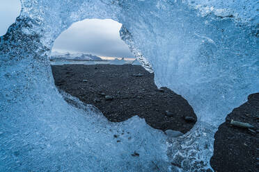 Uneven hole in transparent piece of ice melting in diamond beach in Diamond Beach, Vatnajokull National Park, Iceland - ADSF49685