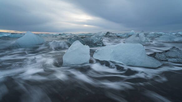 Picturesque scenery of rippling sea water with pieces of broken ice floating against cloudy sky in Diamond Beach in Iceland - ADSF49686