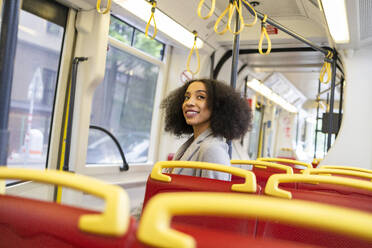 Happy ethnic woman with curly hair standing on city bus while looking up - ADSF49698