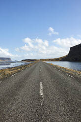 Diminishing perspective of asphalt empty roadway with road markings passing through scenic lake against sky in Iceland - ADSF49712