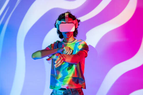A man in a vibrant tie-dye shirt interacts with a virtual world through his VR headset, set against a swirling purple and blue backdrop - ADSF49755