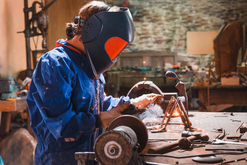 Artisan anonymous sculptor diligently works on a metal sculpture using welding equipment amidst a rustic workshop filled with tools and unfinished projects - ADSF49768