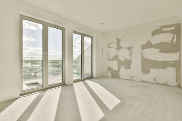 Sunlight falling through large windows in empty unfurnished room with white walls at refurbished apartment - ADSF49772