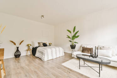 Comfortable bed with sofa and coffee table arranged in spacious apartment with white walls and parquet floor - ADSF49777