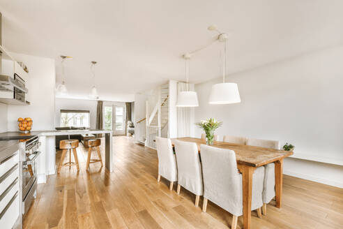 Pendant lights hanging over wooden table and chairs in front of spacious kitchen at contemporary white apartment - ADSF49796