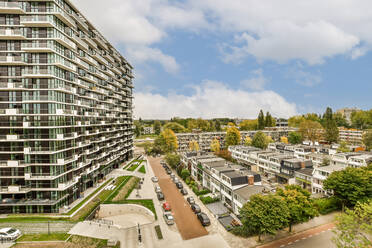 Aerial view of cityscape with modern apartment buildings and parking lot under cloudy sky during sunny day - ADSF49800