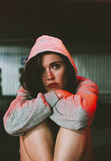 Stressed woman wearing hooded shirt hiding in garage - SVCF00415