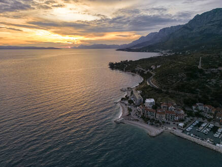 Kroatien, Gespanschaft Split-Dalmatien, Podgora, Luftaufnahme einer kleinen Stadt an der Adriaküste bei Sonnenuntergang - TAMF04028