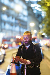 Commuter using mobile phone in city at night - WPEF07886