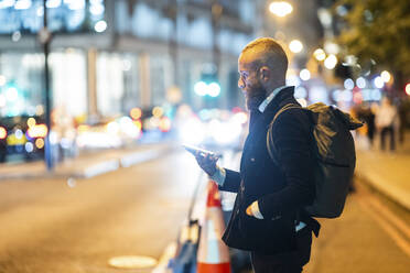 Mann mit Rucksack benutzt Smartphone in der Stadt bei Nacht - WPEF07889