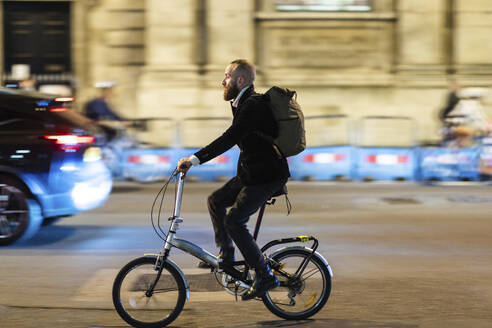 Commuter with backpack cycling on road in city - WPEF07892