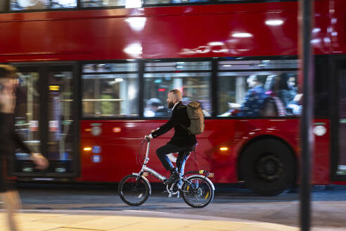 Man cycling near bus in city at night - WPEF07893