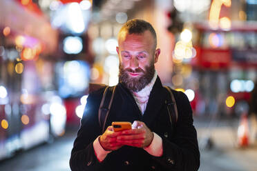 Man using smart phone in city at night - WPEF07894