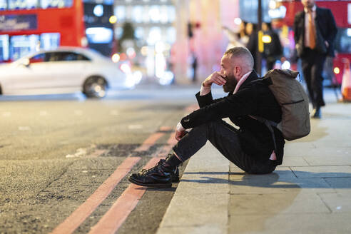 Worried mature man sitting on sidewalk in city - WPEF07898