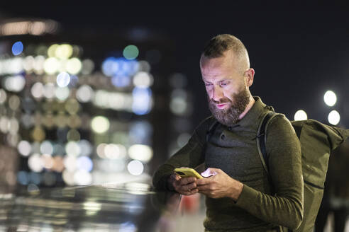 Mann mit Bart benutzt Smartphone in der Stadt bei Nacht - WPEF07899