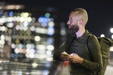 Contemplative man holding smart phone in city at night - WPEF07900