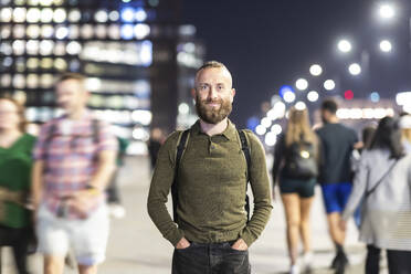 Smiling man standing with hands in pockets in city - WPEF07904