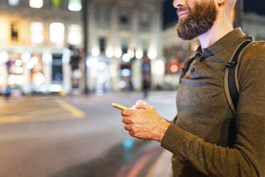 Man with beard holding smart phone in city at night - WPEF07916