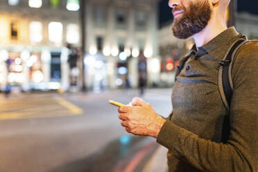 Mann mit Bart hält Smartphone in der Stadt bei Nacht - WPEF07916