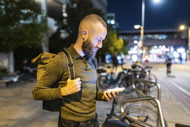Mann benutzt Smartphone in der Nähe eines Fahrradständers in der Stadt bei Nacht - WPEF07918