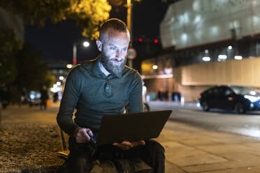 Freelancer using laptop sitting on bench in city - WPEF07921