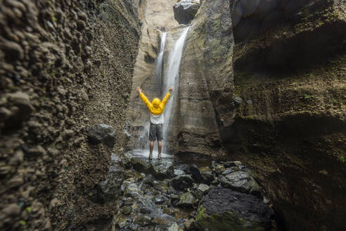 Unbekümmerter Mann steht mit erhobenen Armen vor einem Wasserfall - WVF02044