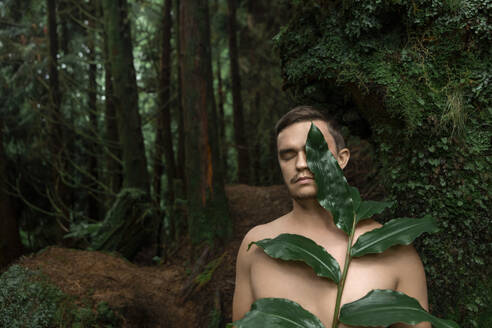 Hemdloser Mann mit Blättern in der Nähe von Bäumen im Wald stehend - WVF02063