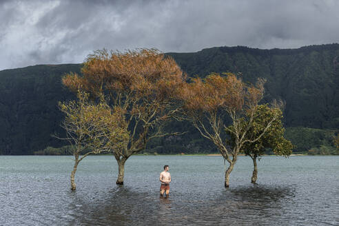 Mann ohne Hemd steht unter Bäumen in einem See in der Nähe von Bergen - WVF02065