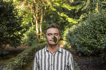 Junger Mann mit Blatt über dem Gesicht im Wald - WVF02088