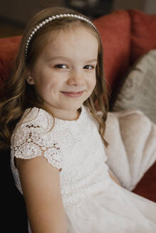 Smiling girl wearing white dress and sitting on sofa - EHAF00129