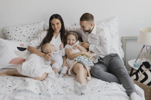 Glückliche Eltern mit Kindern, die zu Hause auf dem Bett sitzen - EHAF00138