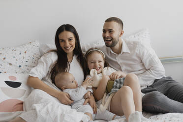 Smiling parents with children having fun on bed at home - EHAF00139