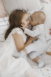 Smiling sister lying and embracing brother on bed - EHAF00141