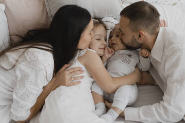 Loving parents kissing cheeks of children on bed at home - EHAF00143