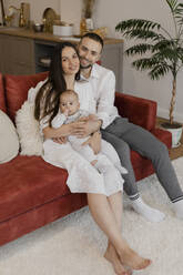 Glückliche Eltern sitzen mit ihrem Sohn auf dem Sofa zu Hause - EHAF00145