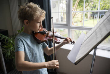 Junge im Grundschulalter übt zu Hause am Fenster Geige spielen - NJAF00683